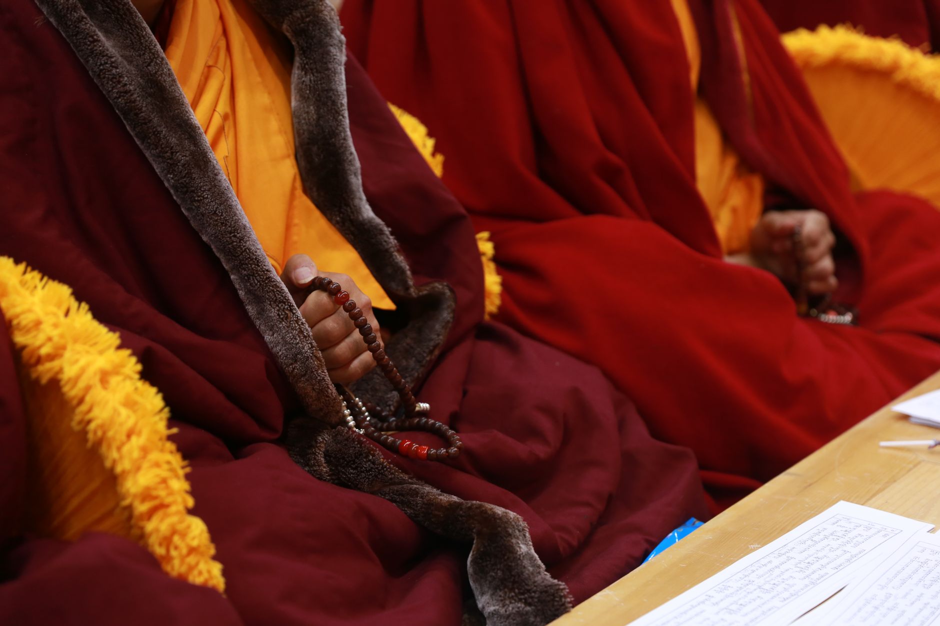 Unrecognizable crop male monks with beads sitting at table in religious oriental clothes