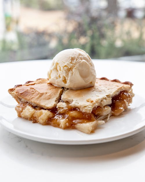 Piece of homemade apple pie served with scoop of vanilla ice cream on plate on white table