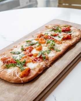 From above of tasty pizza pie served on wooden cutting board on table in kitchen