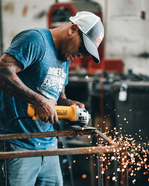 A Man in Blue Crew Neck T-shirt Grinding a Steel Frame