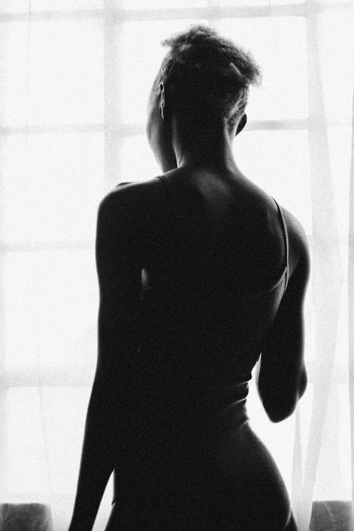 Back view of black and white female silhouette in underwear standing against window