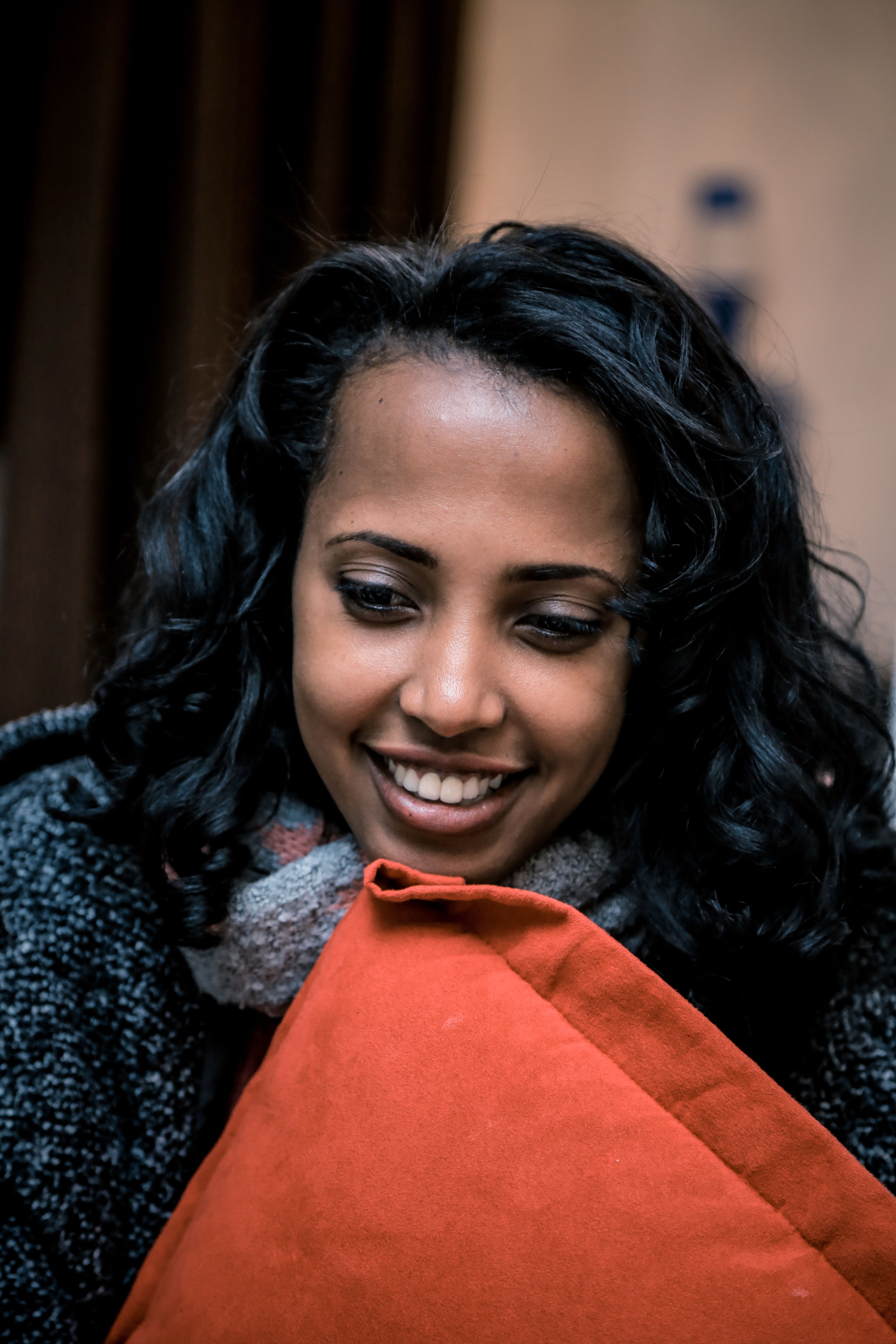 Portrait of a smiling woman with curly hair holding a bright pillow, set against a blurred background.