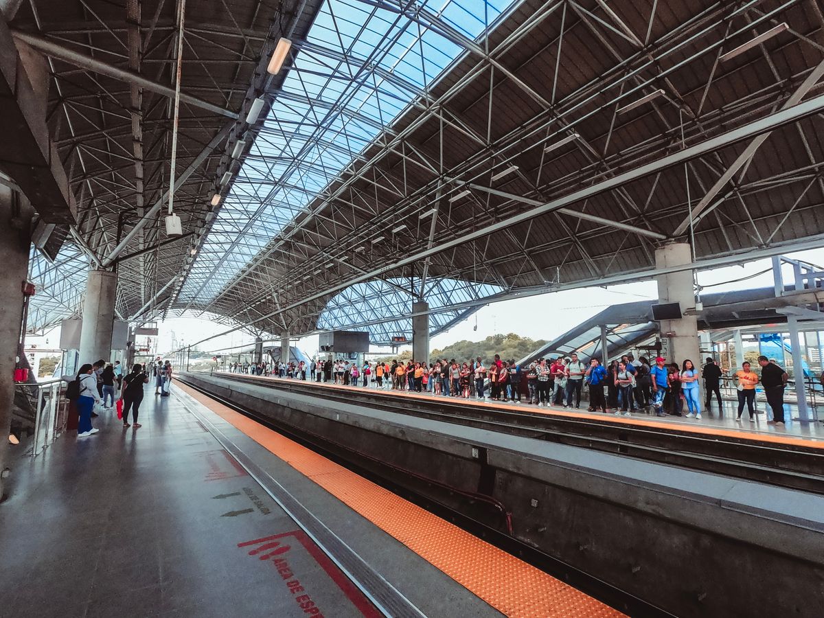 A busy train station platform filled with passengers waiting under a modern glass ceiling