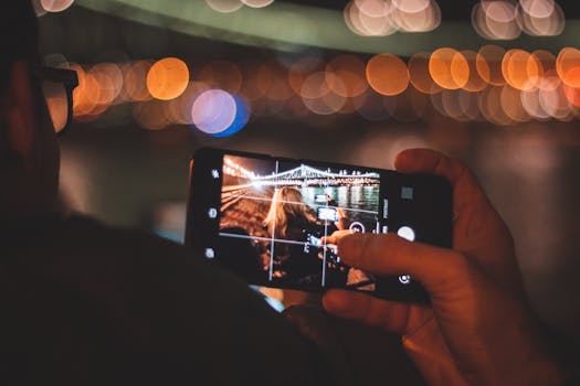 A person capturing a bokeh-lit cityscape using a smartphone at night.