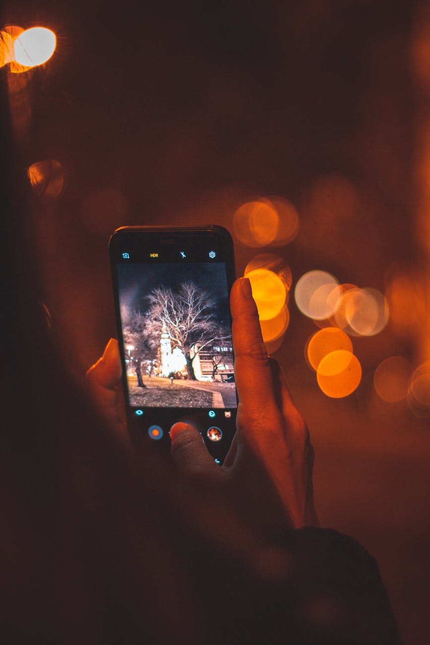 A hand holding a smartphone capturing a glowing building at night.