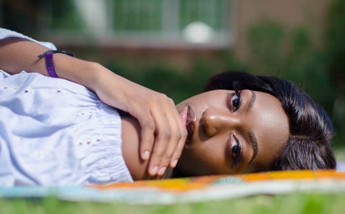 Free Beautiful woman lying on grass, gazing sideways with a serene expression outdoors in summer. Stock Photo