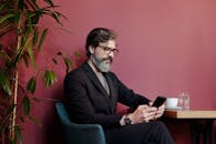 一个留着胡子、戴着眼镜的时髦人士正在现代咖啡馆里使用智能手机