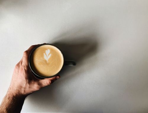 Free A close-up shot of a hand holding a cup of latte with heart-shaped latte art on a white background. Stock Photo