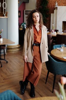 Confident woman poses in modern blazer and pants, showcasing fashionable style indoors.