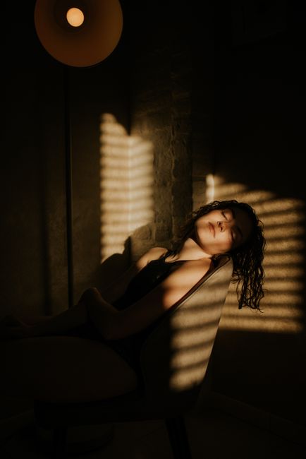 Woman sitting in a chair with sunlight casting shadows, creating a peaceful mood.
