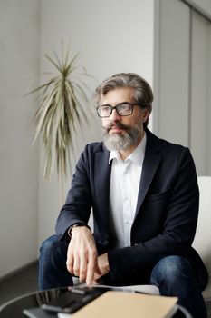 办公室里坐着一位自信的商人，他戴着眼镜，留着胡子，穿着漂亮的西装