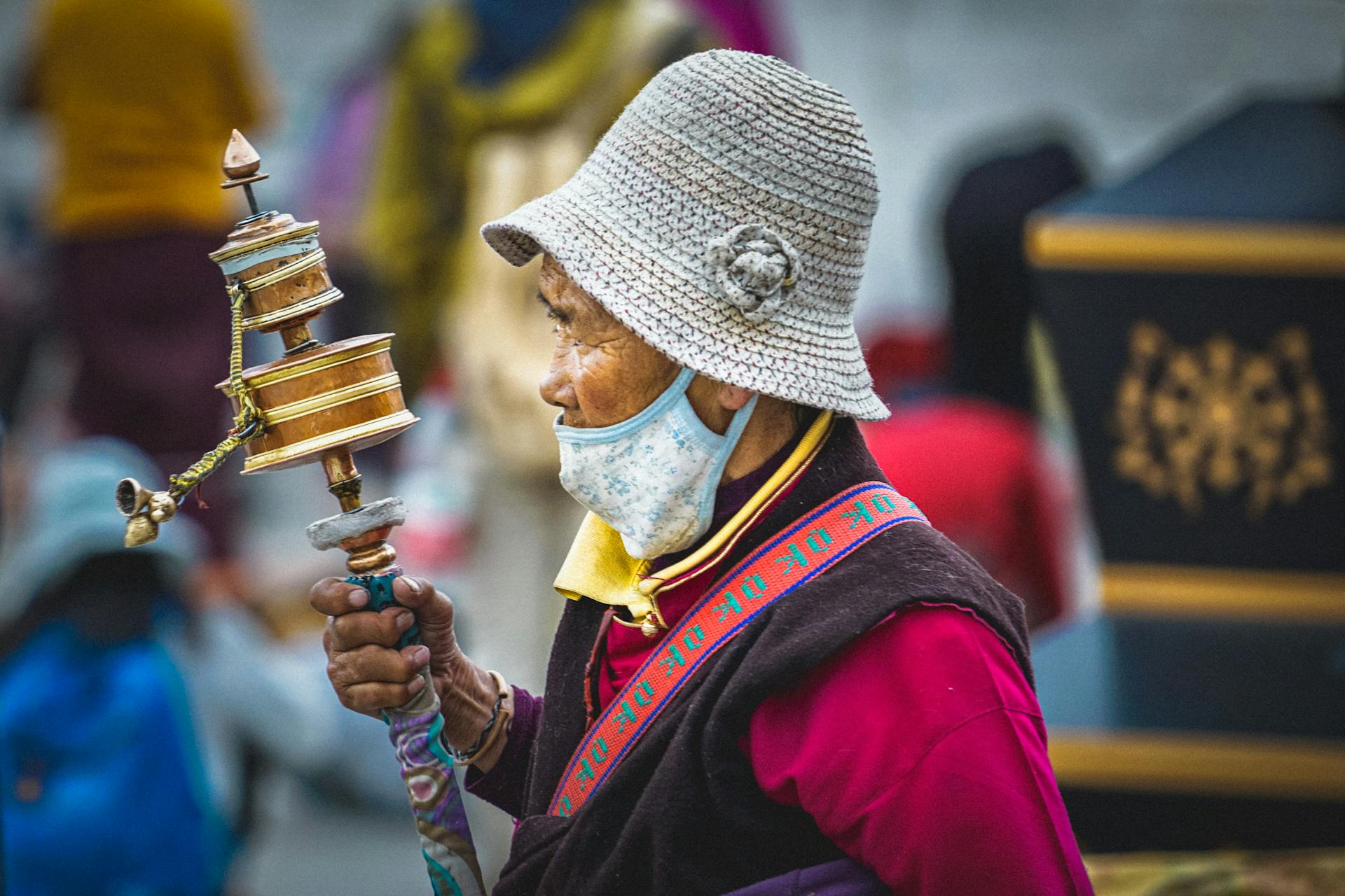 Person i ansiktsmask som håller ett tibetanskt buddhistiskt bönshjul