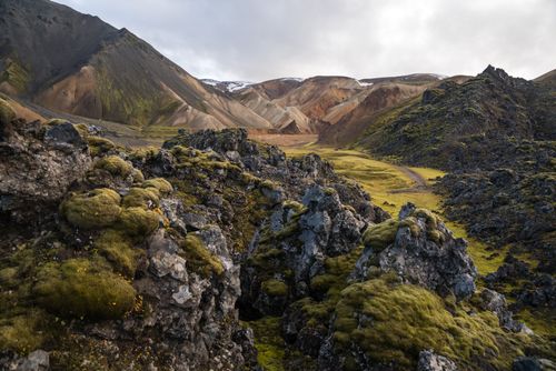 Free Magnificent view of dark rocks partially covered with light green moss and terrain surrounded by sandy mounts under sky with low clouds Stock Photo