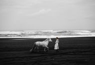 Unrecognizable woman walking with gray stallion on sea beach
