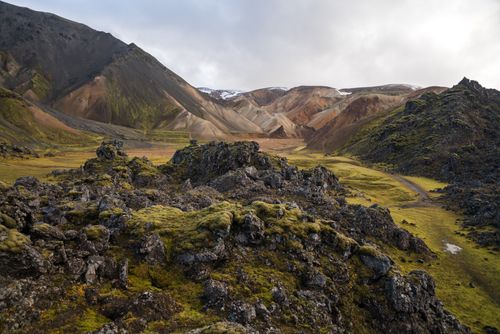 Free Magnificent view of green meadow between sandy mounts and dark rocky formations with bumpy surface under white sky in daylight Stock Photo