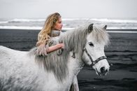 Woman caressing gray stallion on beach near ocean in daylight