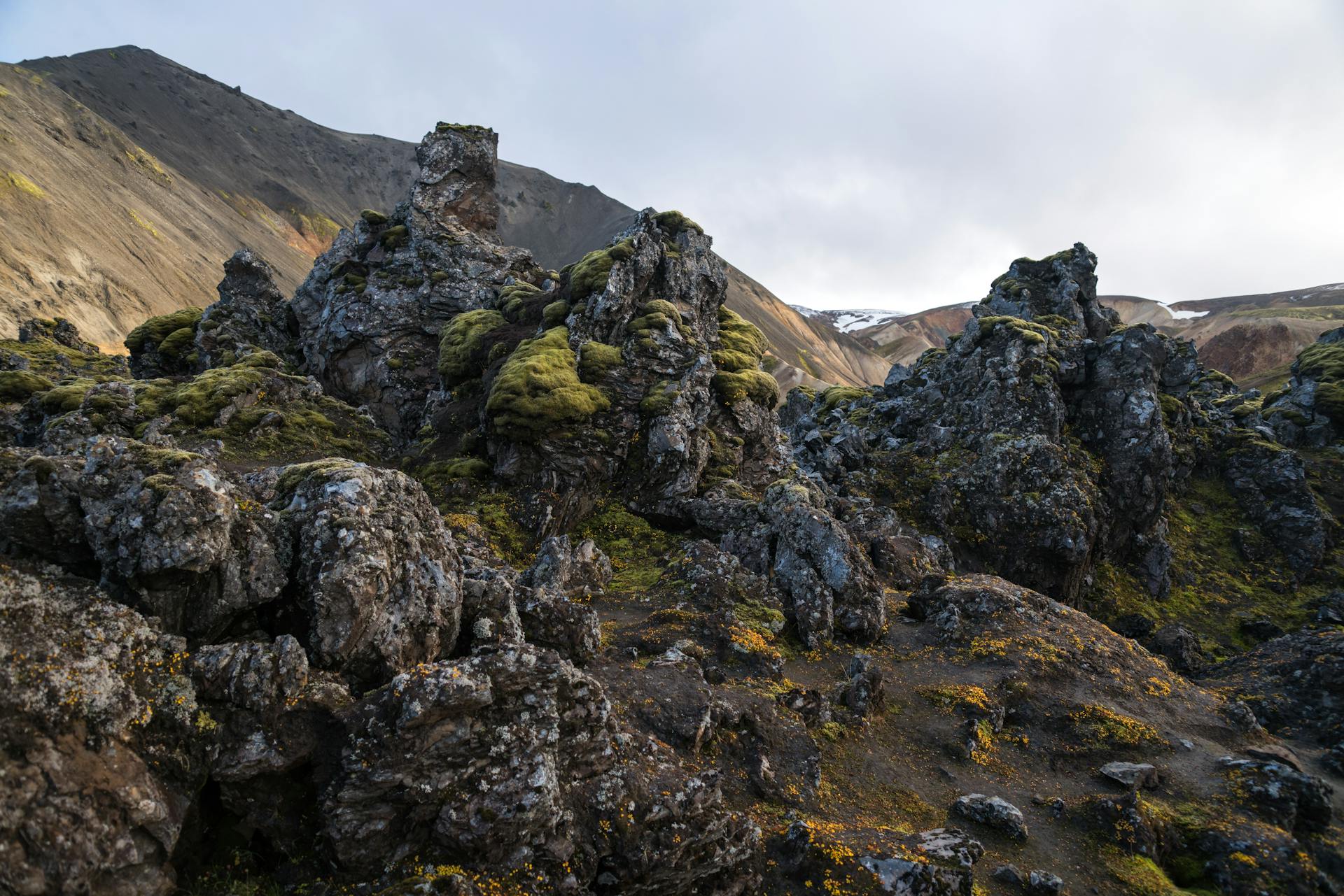 Majestic view of sandy ridge and pointed dark gray rocks with uneven shabby surface and solid structure partially covered with moss under cloudy sky in daylight