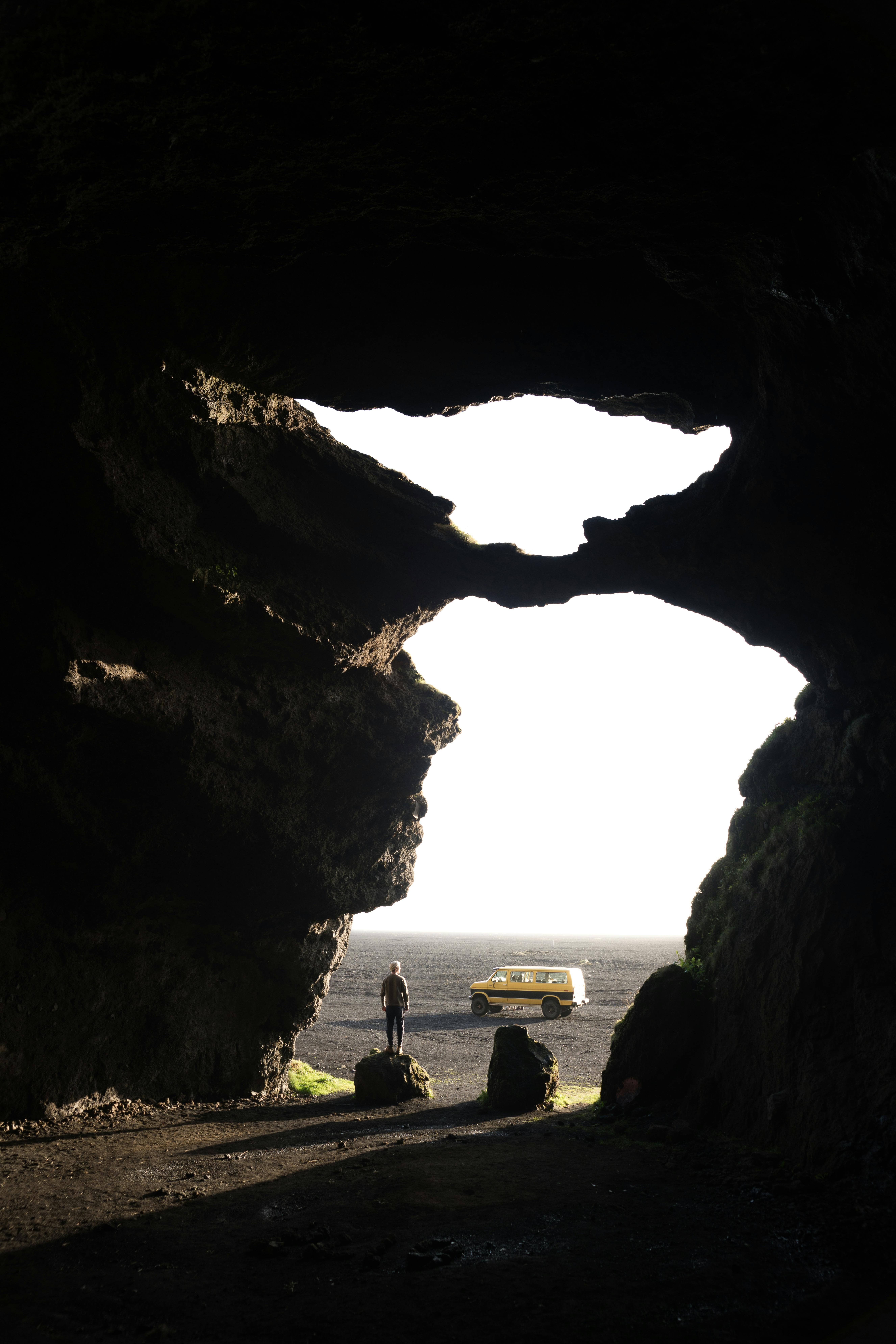Anonymous man standing on boulder in cave entrance with unusual shape against jeep during trip to famous tourist location