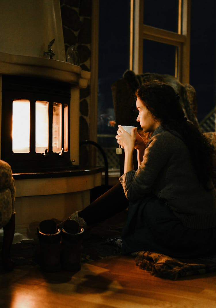 Tranquil Young Woman Drinking Tea In Front Of Fireplace