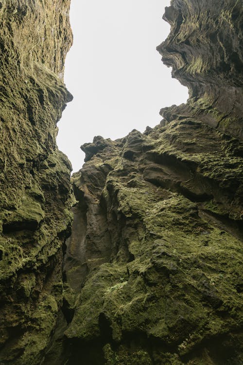 From below amazing view from ravine of severe rough rocky mountain covered with green moss and lichen during cold day