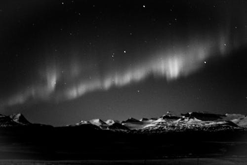 Black and white of snowy remote mountain peaks under dark sky with polar lights in winter night