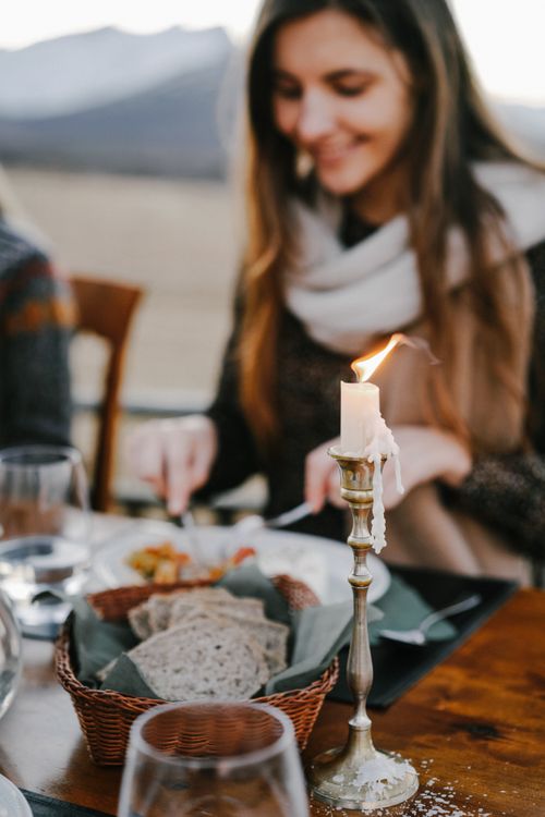 Free Young lady in warm clothes sitting at table with burning candle and wicker basket of bread while resting in outdoor cafe during romantic dinner at evening Stock Photo