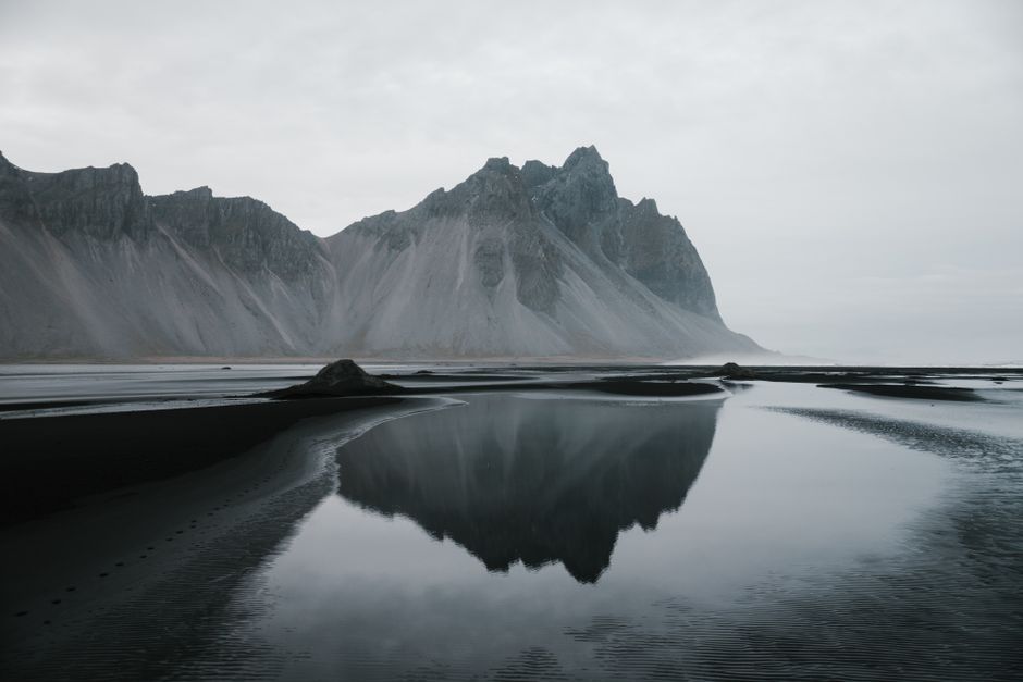 Amazing mountain range located on coast lake and reflected in calm water against cloudy sky in overcast weather
