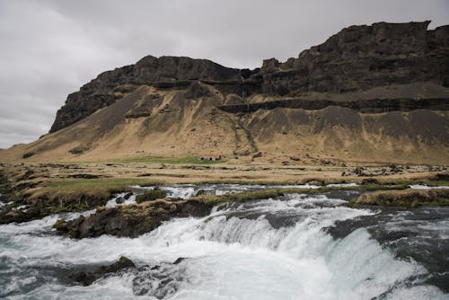 Amazing view of mountain ridge and rapid river flowing through rocky valley in highland and small waterfall in overcast weather