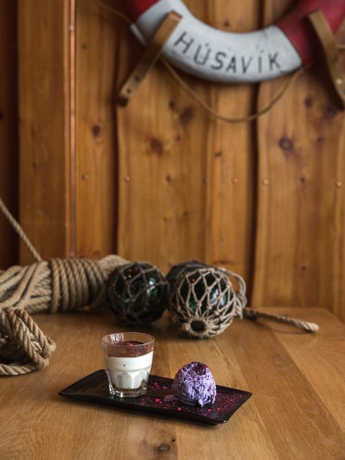 Free From above of ceramic plate with dessert in glass with chocolate top and ice cream scoop garnished with pink dye placed on wooden table against knot of rope and glass balls in grid and lifebuoy on wall Stock Photo