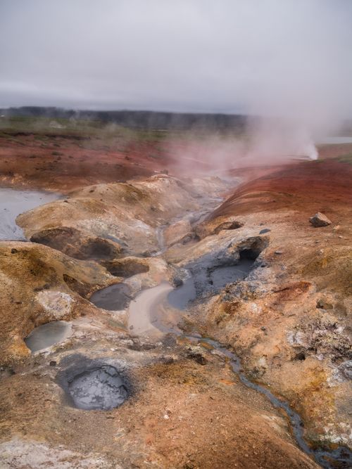Free Hilled country with geysers doing steam among hot springs and holes with mud against mountains in evening in cloudy weather Stock Photo