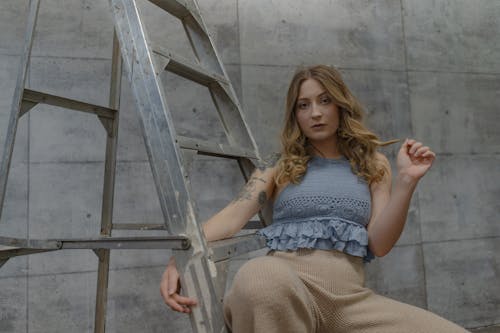 Woman Wearing a Blue Crop Top Sitting on Gray Ladder