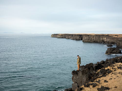 Man standing on rocky cliff near calm sea