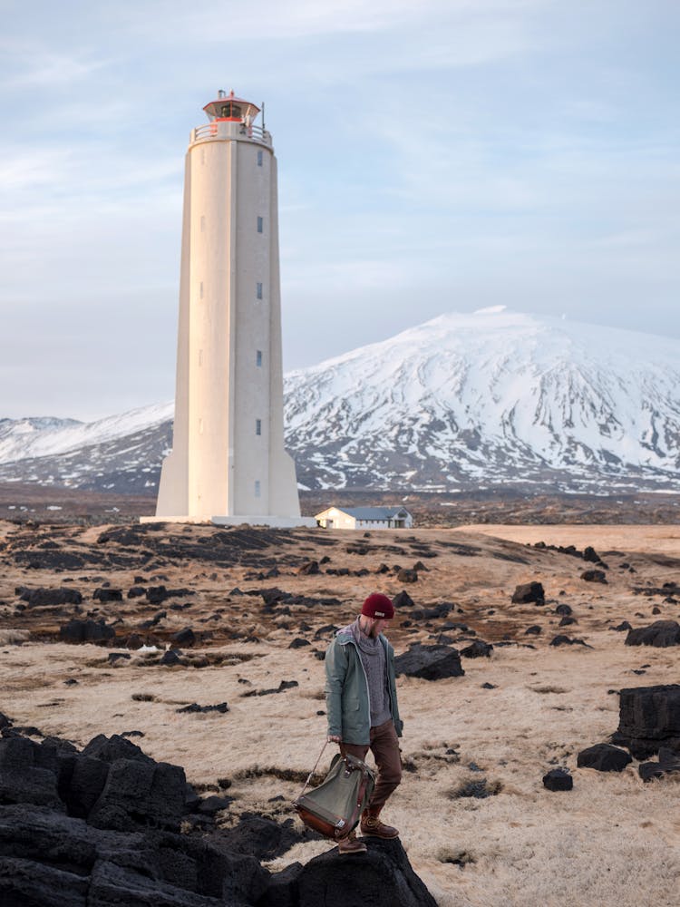 Man Walking Near Lighthouse And Snowy Mountain