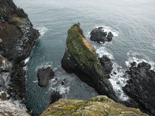 Free From above breathtaking scenery of rough rocky green cliff washed by calm blue sea water crashing against rocky shore Stock Photo
