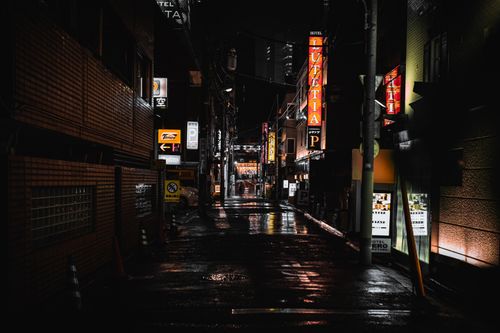 Free A dark, wet alley in Tokyo, Japan, illuminated by colorful signs at night. Stock Photo