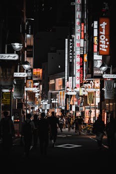 A vibrant night scene captures the bustling streets of Tokyo, Japan, with bright signages and people walking.
