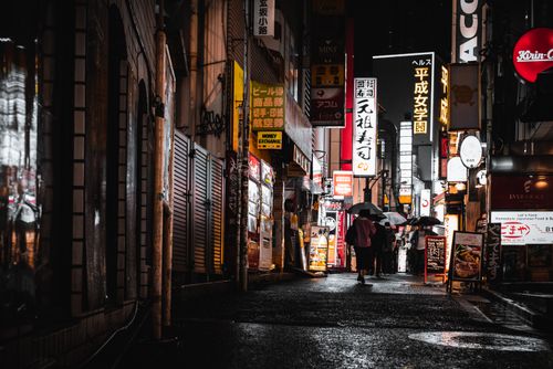 Free People walking under umbrellas in Tokyo's neon-lit streets at night, capturing the city's vibrant urban life. Stock Photo