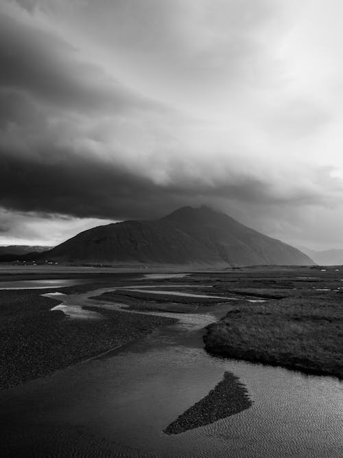 Picturesque black and white view of dark cloudy sky over mountain and narrow curvy river on rocky highland