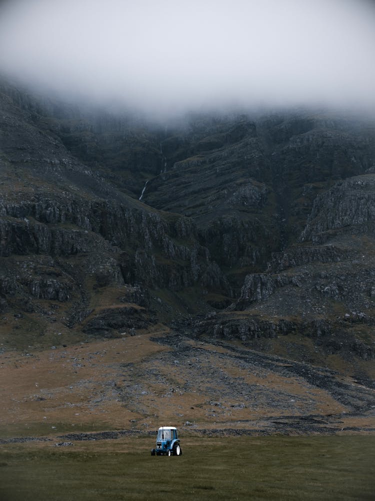 Solitary Tractor On Green Highland Valley Near Mountains