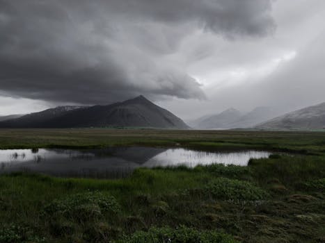 Majestic view of rough mountainous terrain with green valley and cold lake under gloomy dark cloudy sky