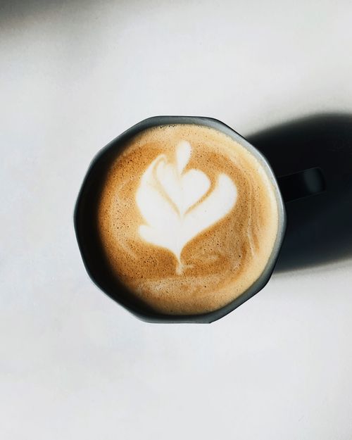 Free Aerial shot of a latte with heart-shaped art in a black mug on a white background. Stock Photo