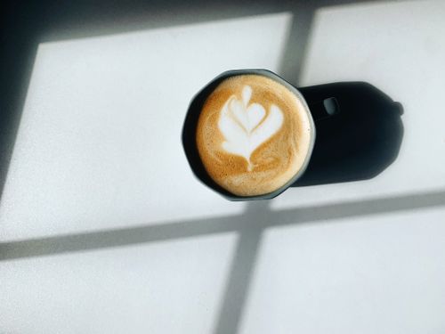 Free A close-up of a latte with heart-shaped foam art, casting a shadow on a bright surface. Stock Photo