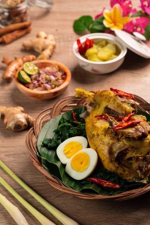Free Eggs and meat in wicker basket composing with ginger root and small delicate flowers on table in bright room in daylight Stock Photo