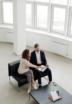 Two professionals discussing work on a laptop in a modern office environment.