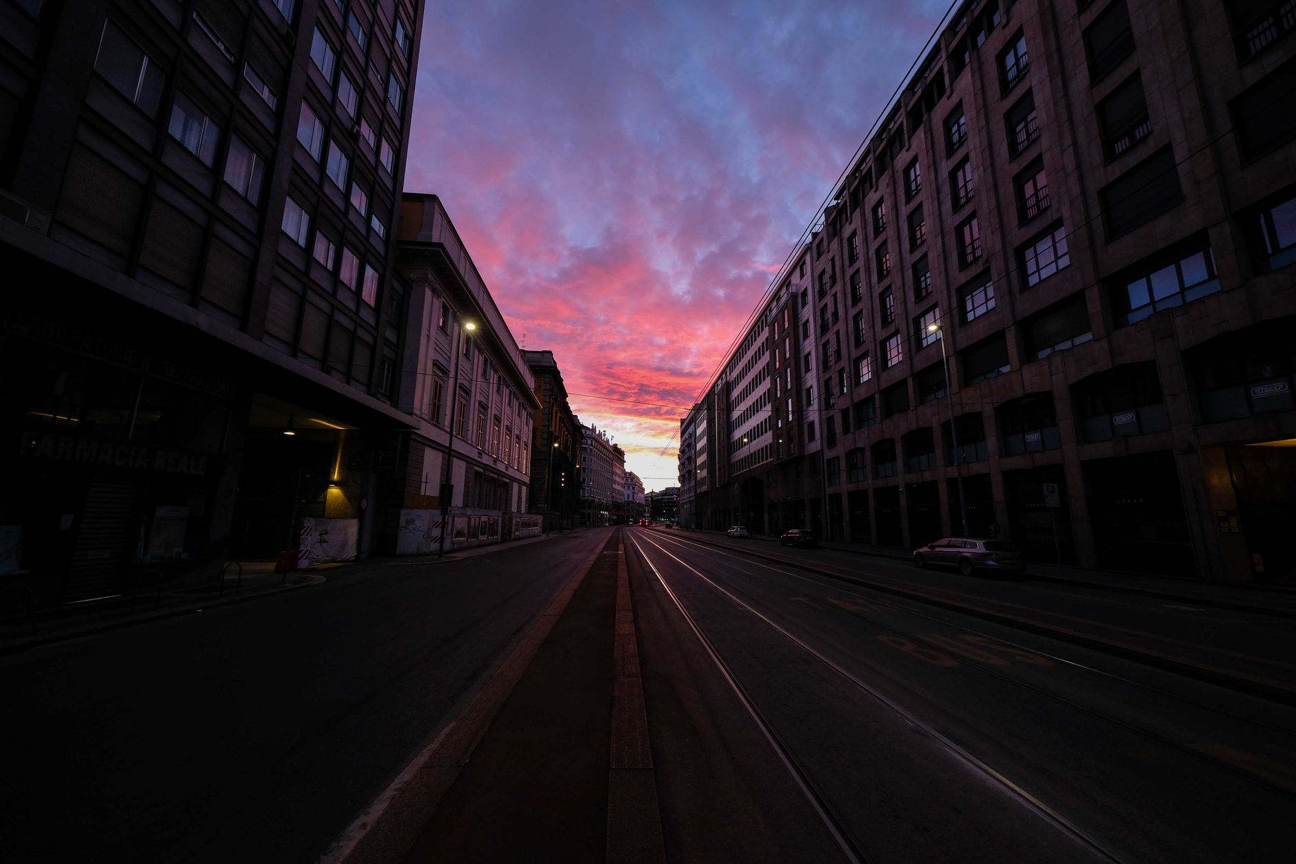 Colorful sundown above railroad on empty street surrounded by high buildings in evening