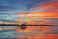 平静的海面上，船只和小屋映衬着日落鲜明的色彩