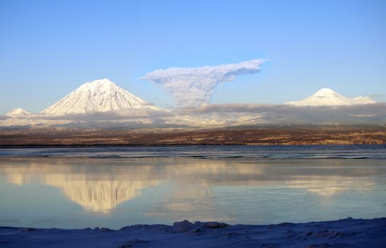 A serene view of snow-capped volcanoes reflecting in a tranquil lake at dawn.