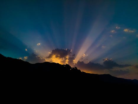 Beautiful sunset with dramatic sunbeams illuminating clouds over silhouetted mountains.