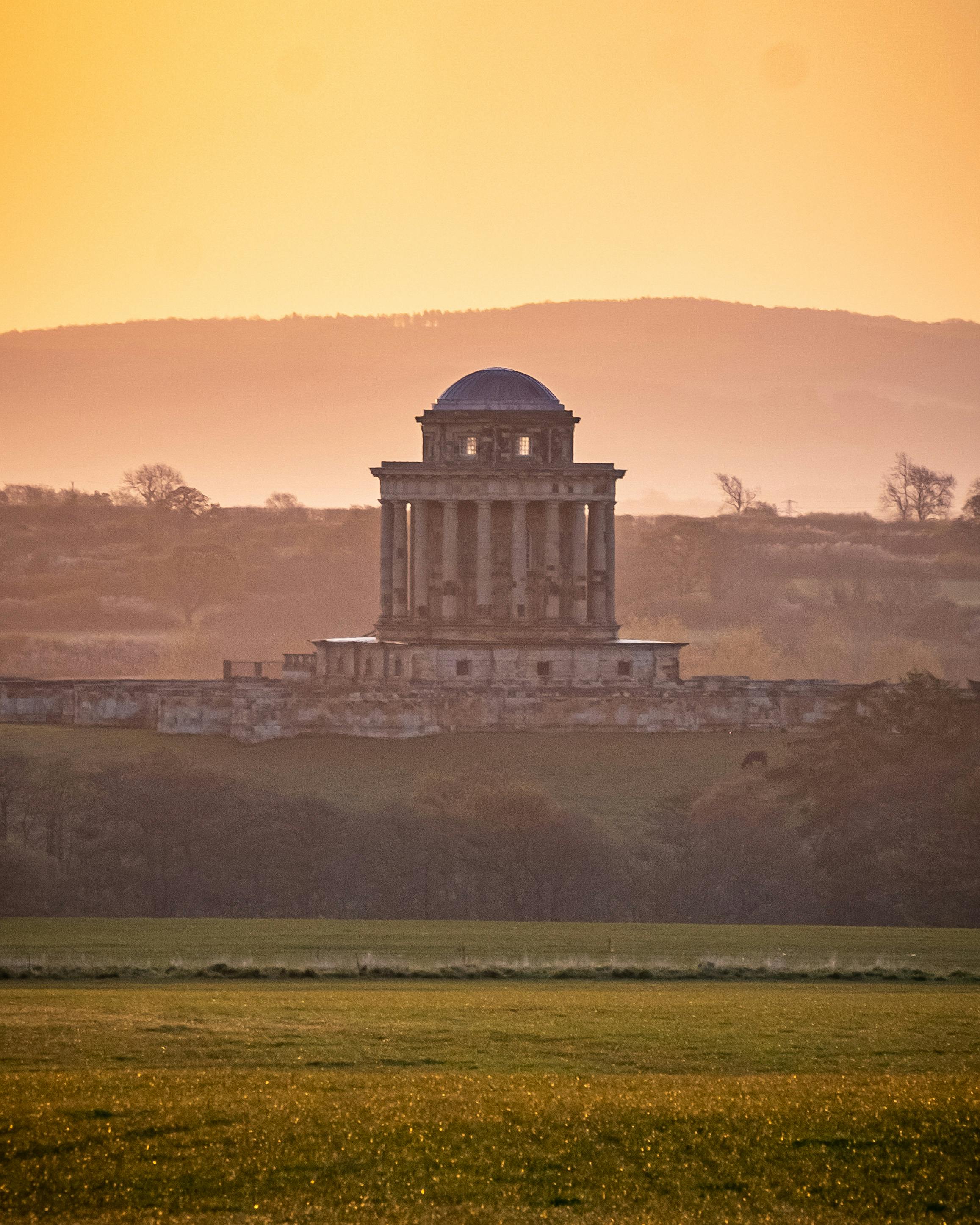 Sunset view of Castle Howard mausoleum, enveloped in golden sunlight and mist.