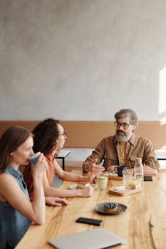 A group of adults discussing and enjoying coffee at a wooden table in a cafe.